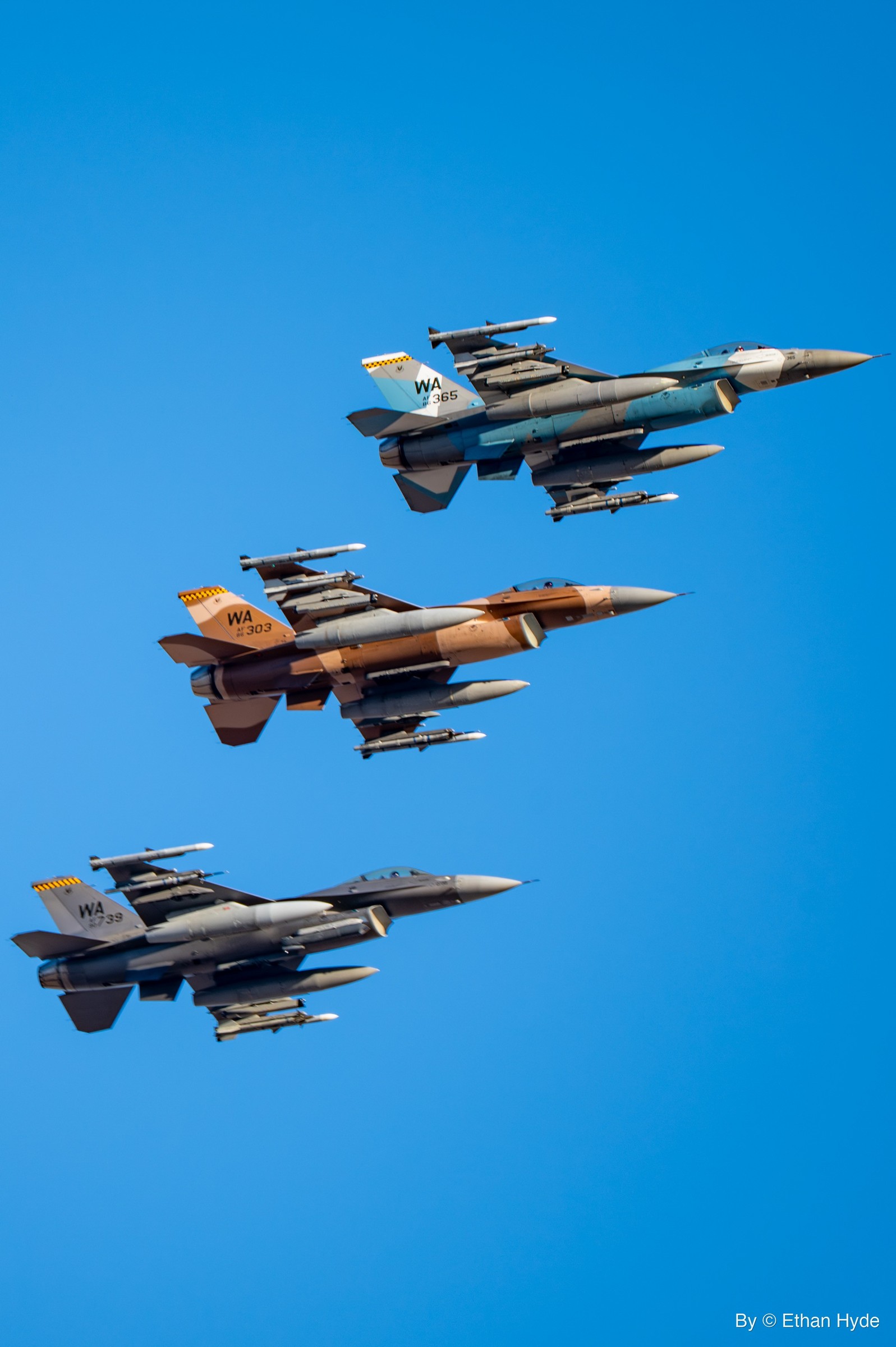 A formation of camouflaged F-16 fighter jets climbing together against blue sky.