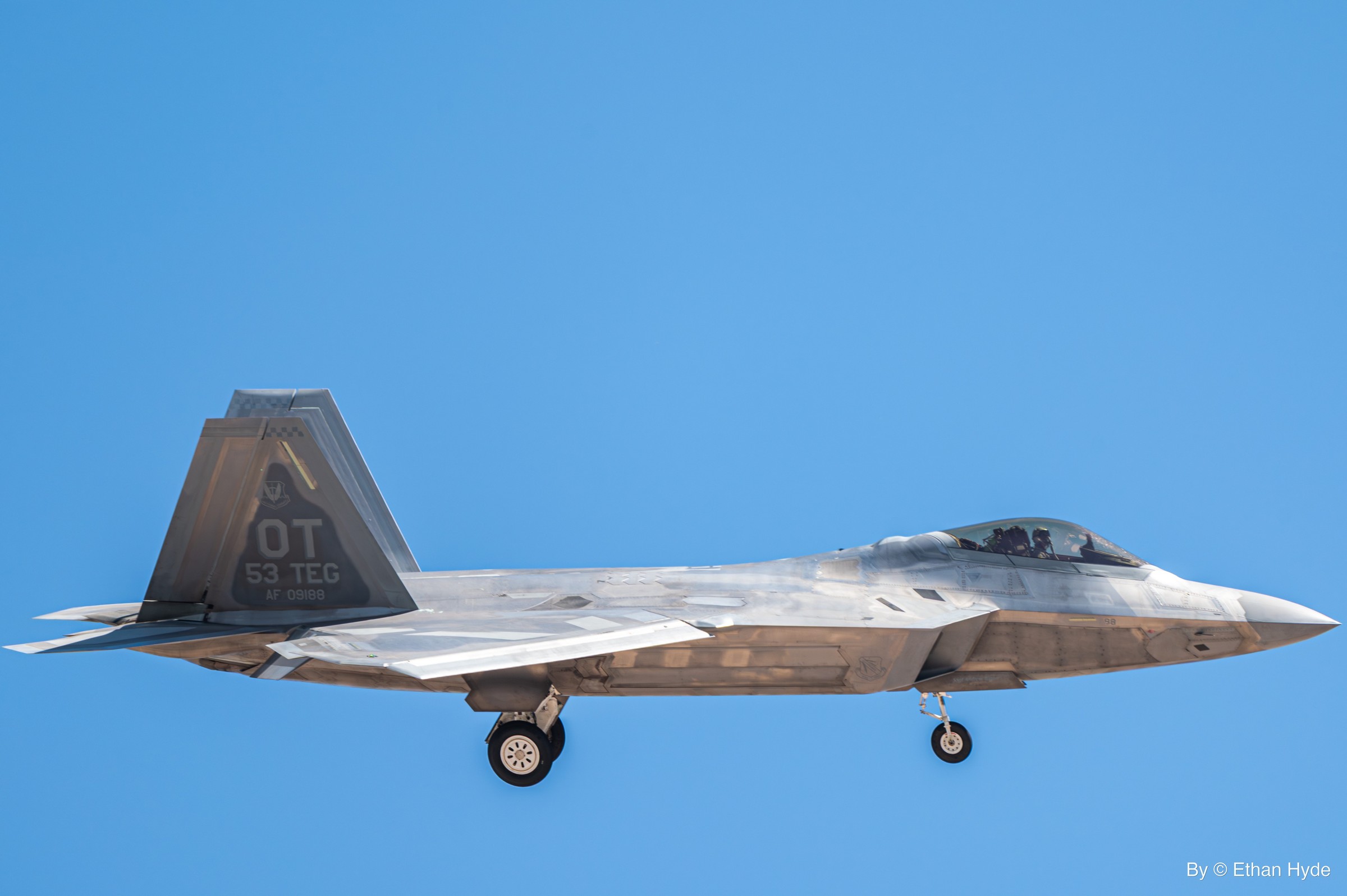 An F-22 Raptor stealth fighter in flight against a blue sky.