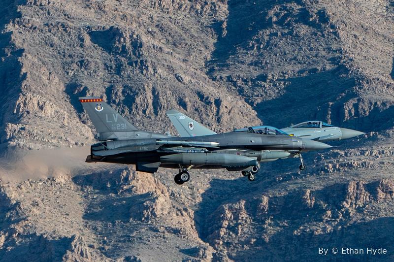A fighter jet flying low through a rugged desert canyon, terrain filling the frame.