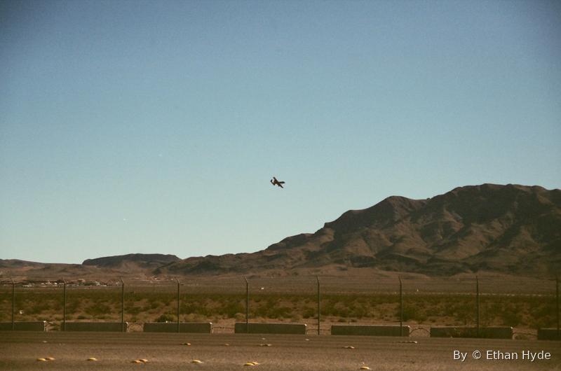 A jet crossing low over a wide desert valley ringed by mountains.