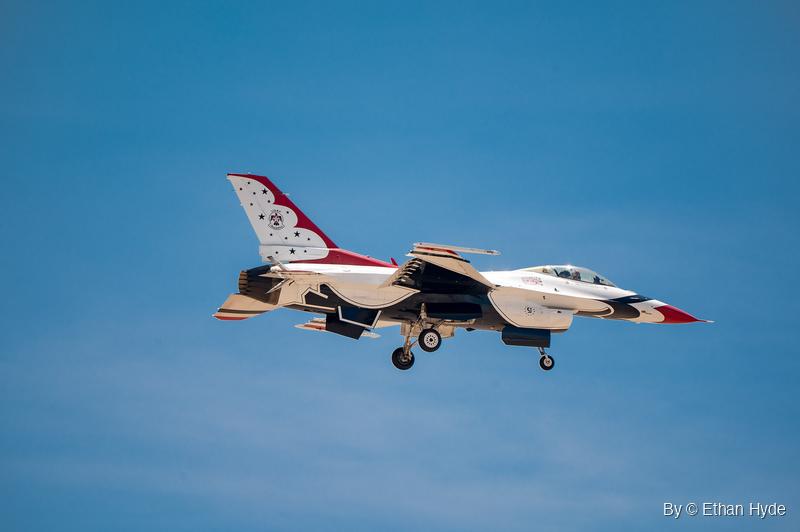 A single F-16 in red, white and blue demonstration paint flies with its landing gear extended against a hazy blue sky.