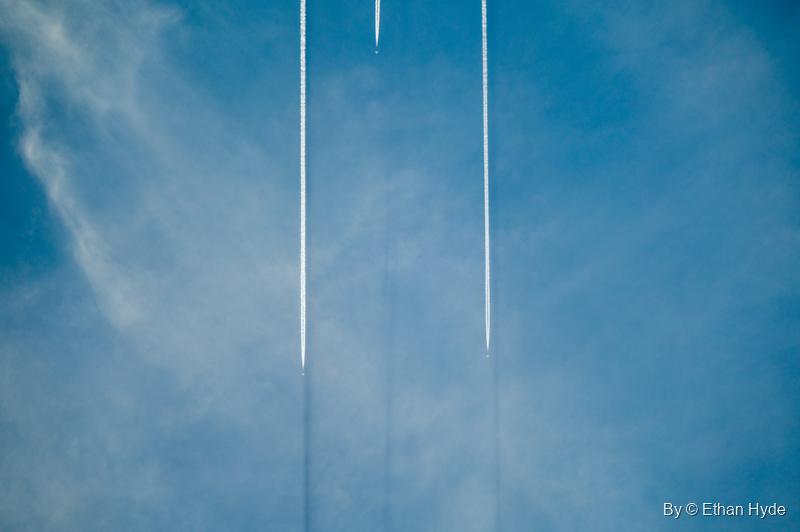 Two straight white contrails run side by side up a blue sky streaked with thin cloud.