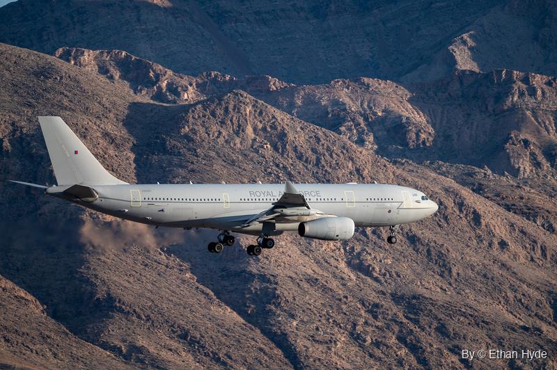 A gray Royal Air Force Voyager tanker flies gear-down past rugged brown desert mountains on approach.