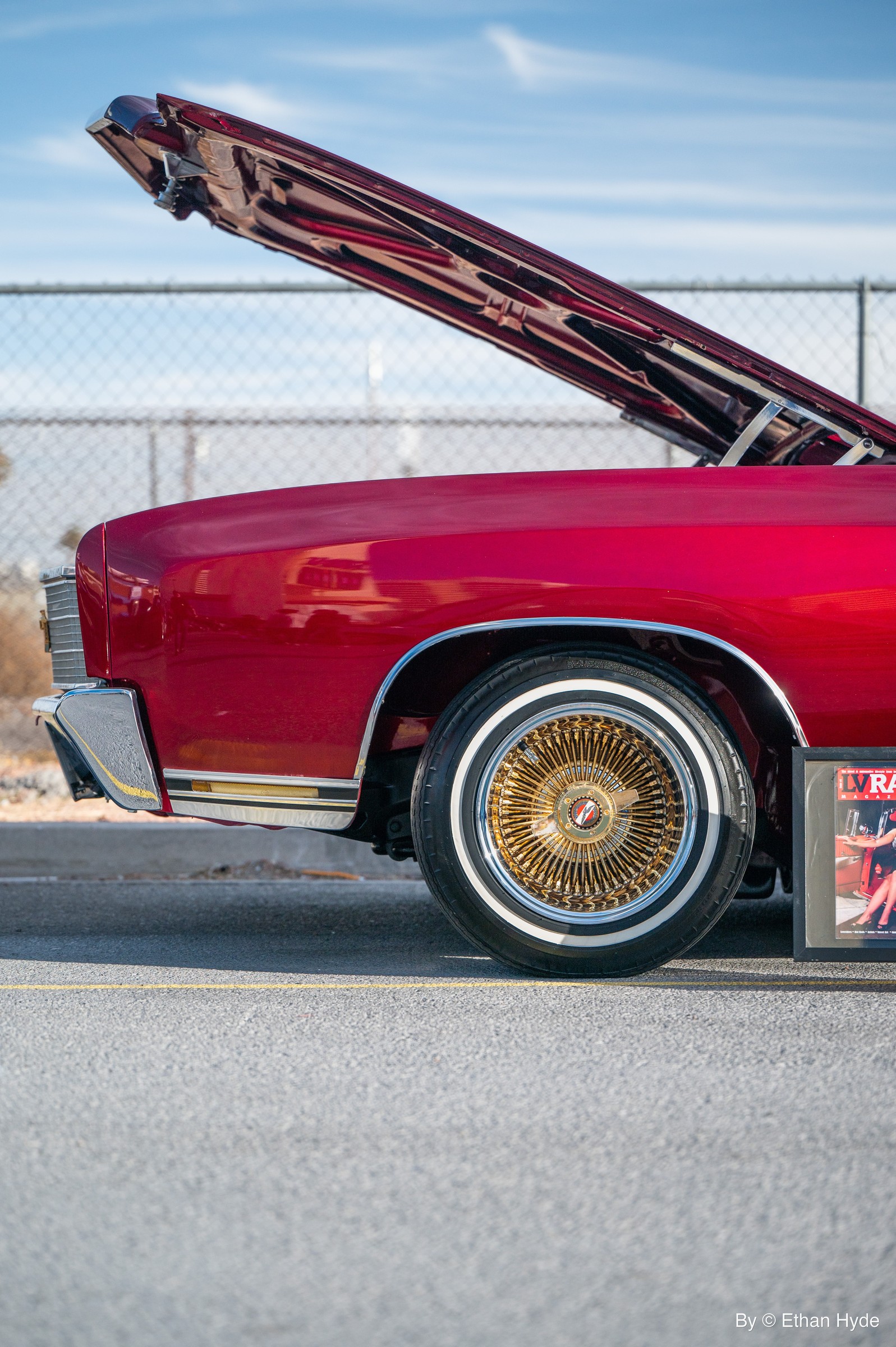 Close-up of a deep-red lowrider with gold wire wheels and whitewall tires.