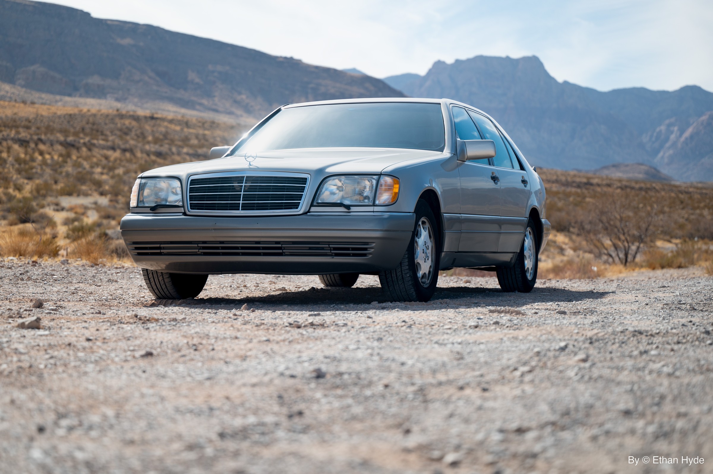 A silver Mercedes-Benz sedan parked on desert gravel below red rock formations.