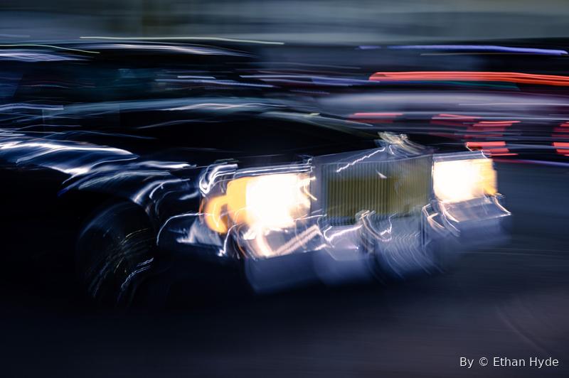 A car at night reduced to streaks of headlight and reflection by a long exposure.