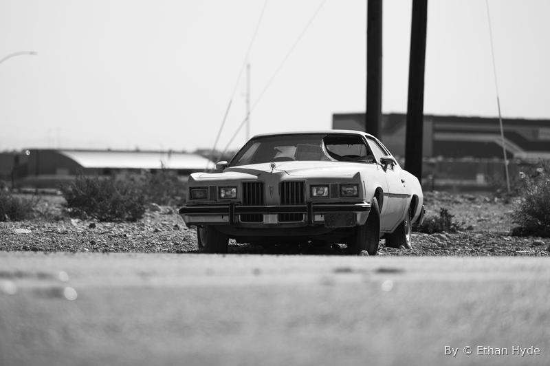 Black-and-white photo of a classic coupe parked on a desert roadside.