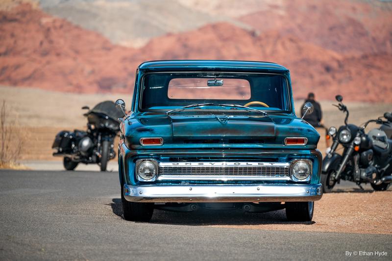 Front view of a turquoise classic pickup with motorcycles parked alongside in the desert.