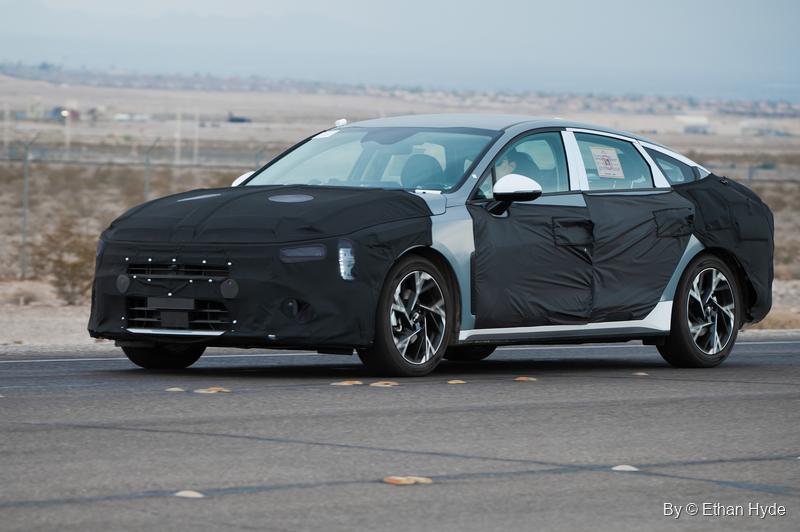 A pre-production sedan wrapped in black and white camouflage cladding drives along a desert test road.