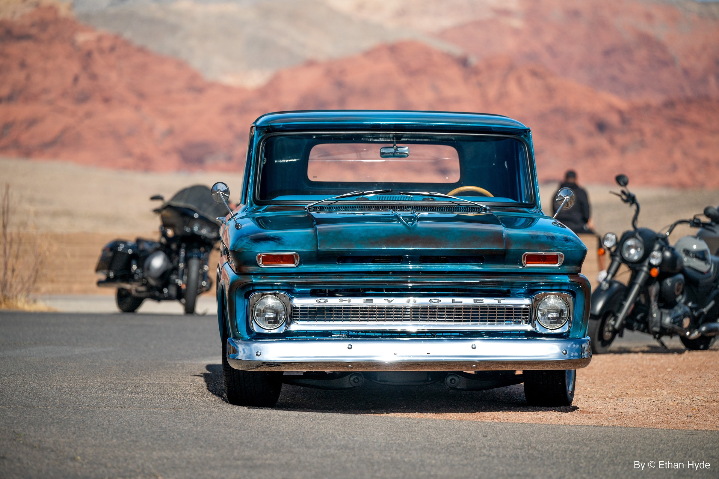 Front view of a turquoise classic pickup with motorcycles parked alongside in the desert.
