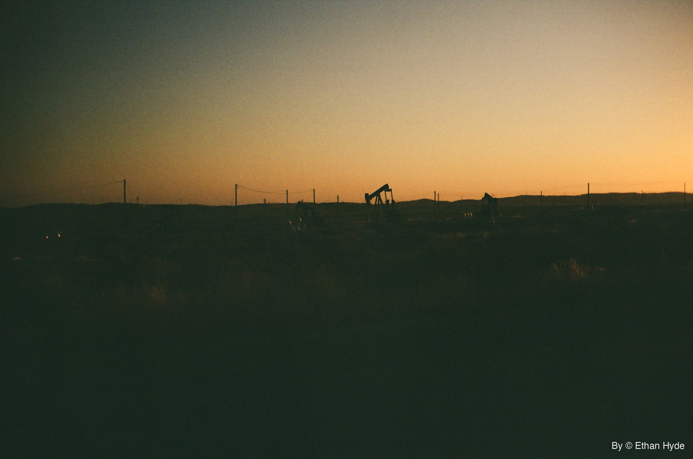 A lone pumpjack on a dark ridgeline under a glowing sunrise near McKittrick, California, shot on film.