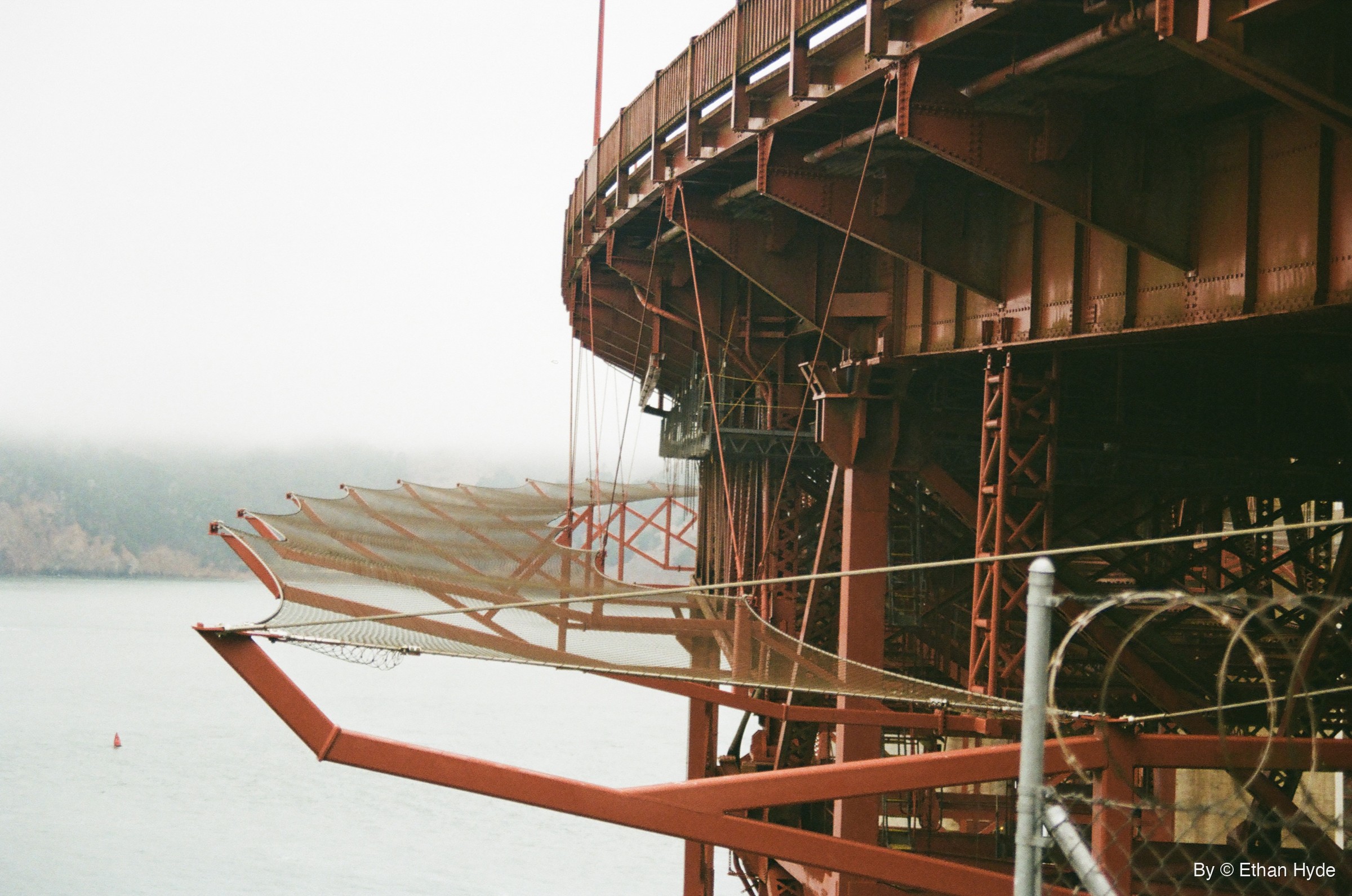 The red steel underside of the Golden Gate Bridge curving out over the bay in fog, shot on film.