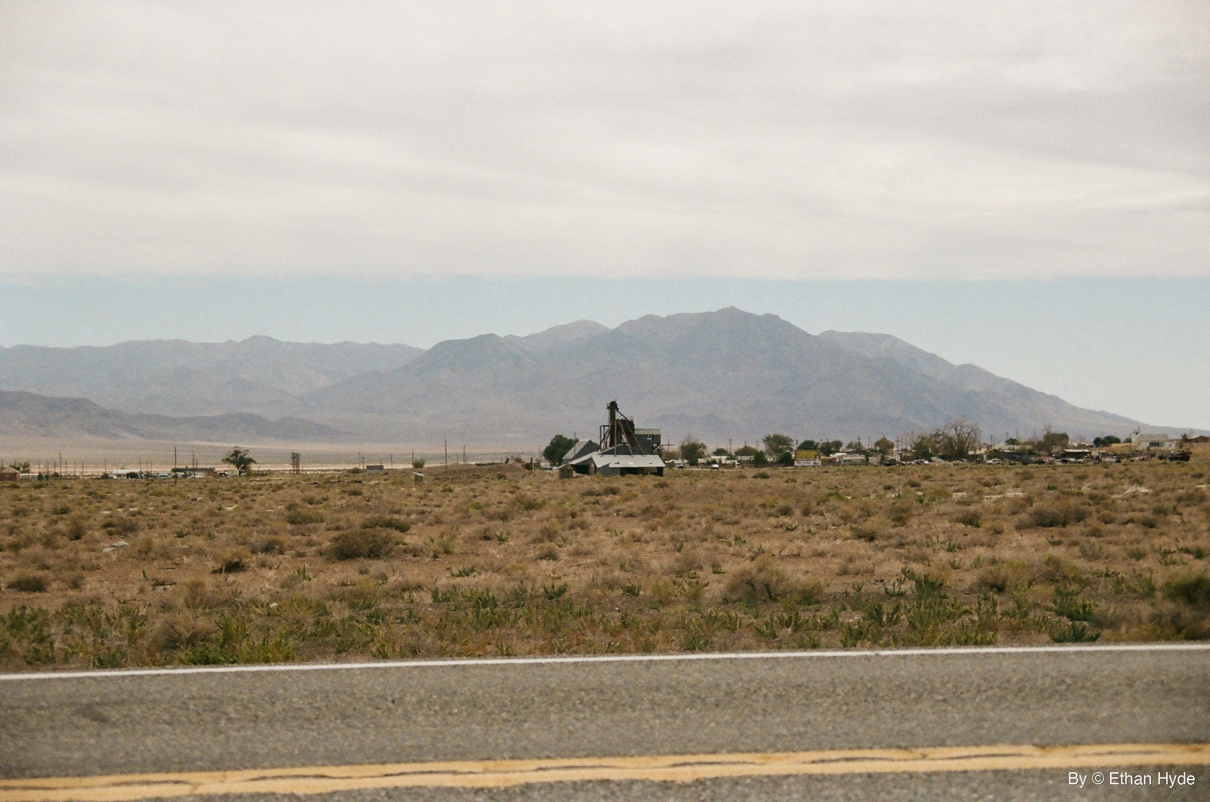 Desert scrub and a few buildings below a hazy mountain range beside the highway at Luning, Nevada, shot on film.