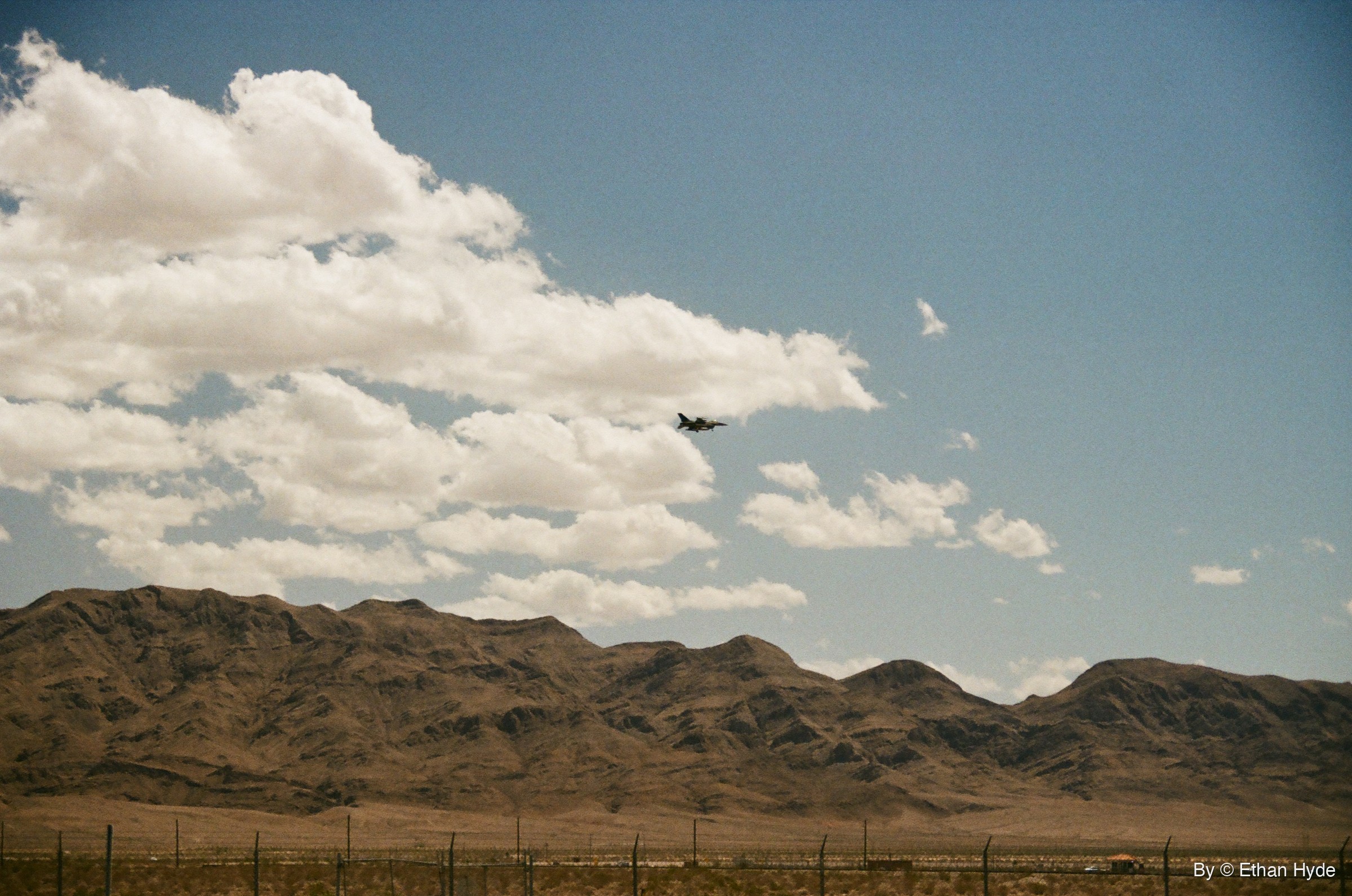 A small fighter jet silhouette against towering cumulus clouds, shot on film.