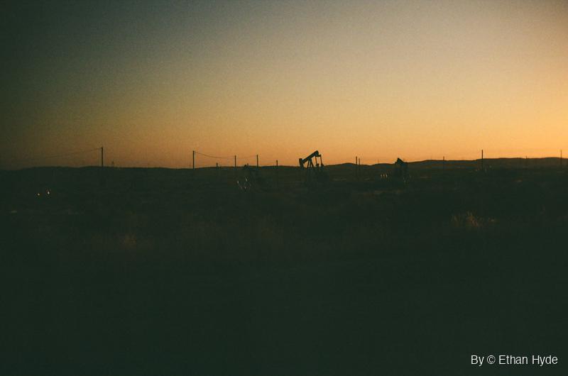 A lone pumpjack on a dark ridgeline under a glowing sunrise near McKittrick, California, shot on film.