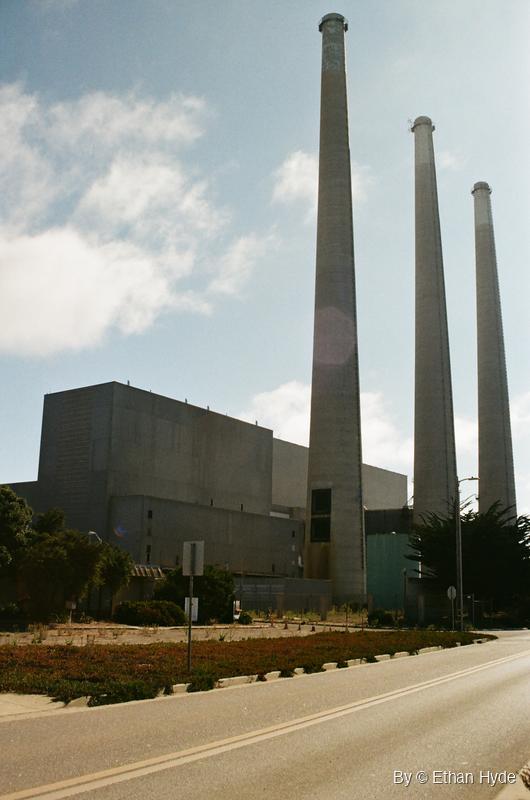 Looking up at the three concrete smokestacks of the Morro Bay power plant against a blue sky, shot on film.