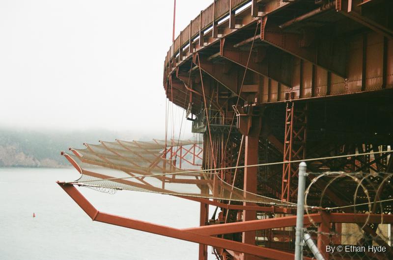 The red steel underside of the Golden Gate Bridge curving out over the bay in fog, shot on film.
