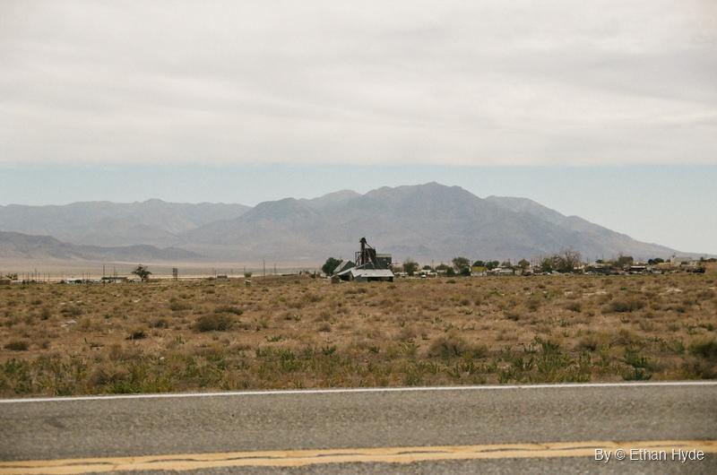 Desert scrub and a few buildings below a hazy mountain range beside the highway at Luning, Nevada, shot on film.