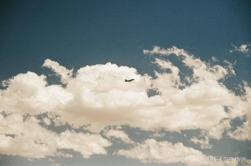 A fighter jet in the clouds above a two-way arrow road sign and desert mountains, shot on film.
