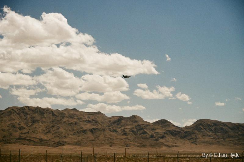 A small fighter jet silhouette against towering cumulus clouds, shot on film.