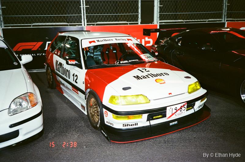 A red-and-white liveried touring race car in a garage, shot on film.