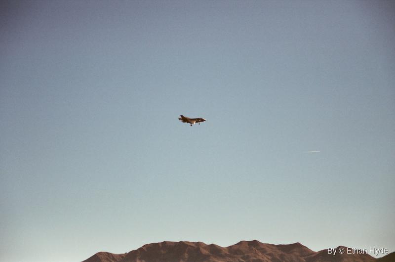 A lone jet over a desert ridge in a pale sky, shot on film.