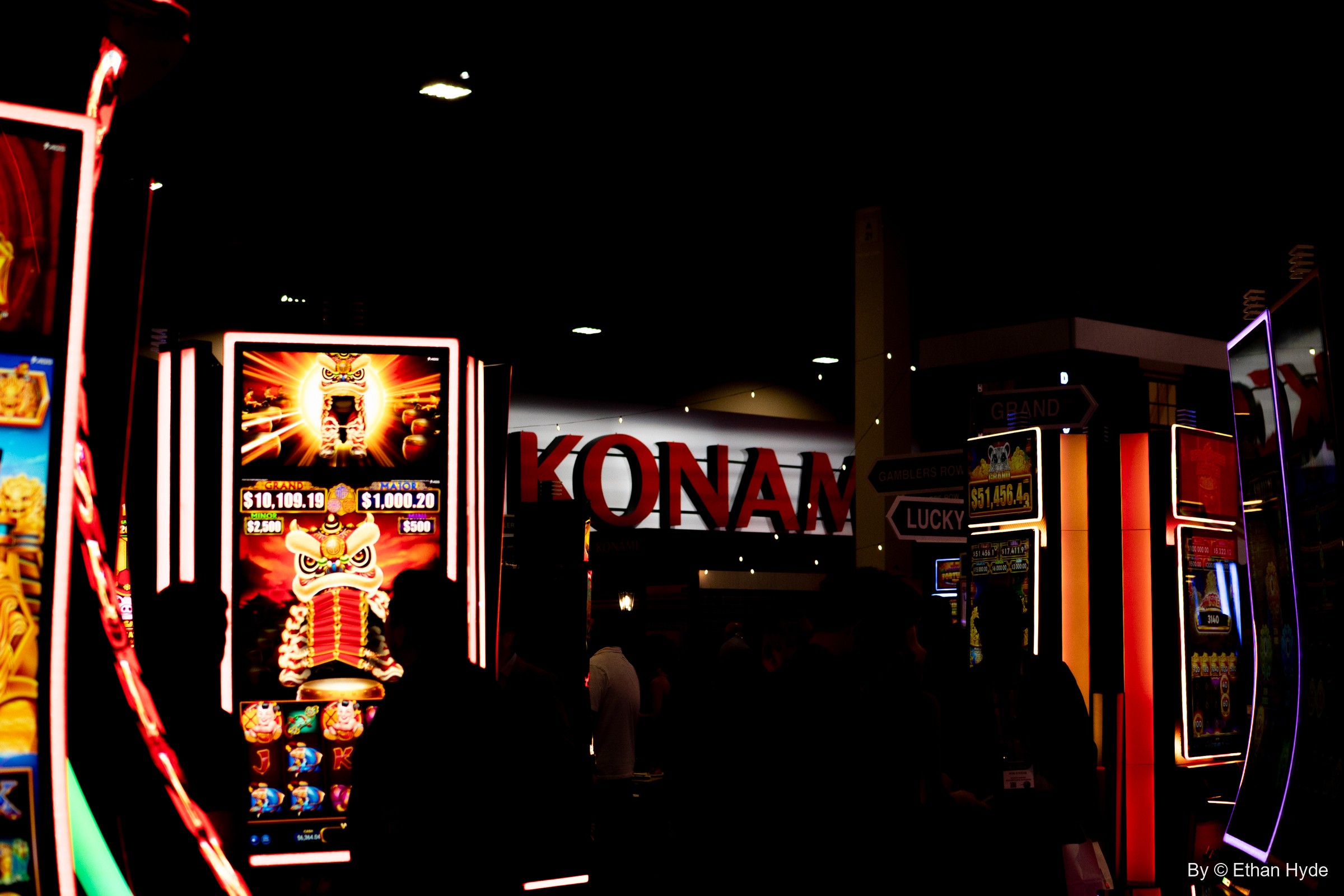 Slot machine cabinets glow around a red Konami sign in a darkened booth at G2E.