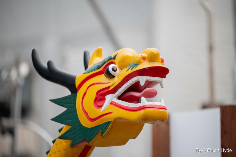 Close-up of a carved yellow, red and green dragon head on a boat prow, mouth open, horns swept back.