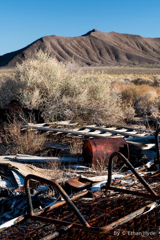 Rusted machinery and metal debris half-buried in desert brush.