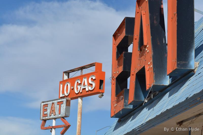 A weathered roadside neon sign reading 'EAT' and 'LO-GAS' against the sky.