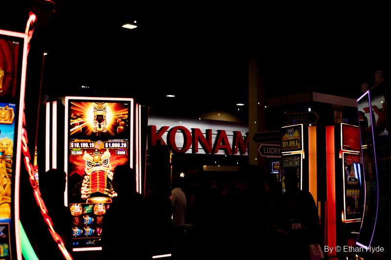 Slot machine cabinets glow around a red Konami sign in a darkened booth at G2E.