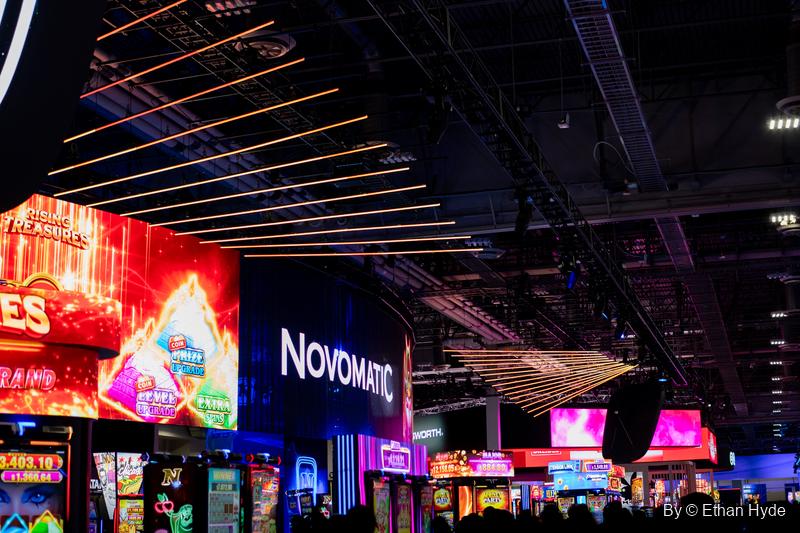 Glowing screens, a Novomatic sign and streaks of ceiling light over the crowded G2E show floor.