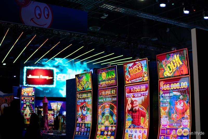A row of brightly lit slot machine cabinets with jackpot displays under strips of colored light at G2E.