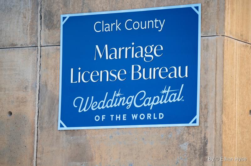 A blue sign reading "Clark County Marriage License Bureau, Wedding Capital of the World" on a concrete wall.