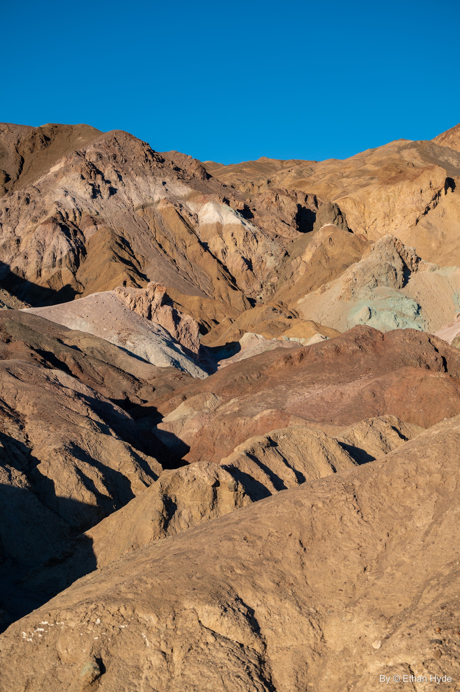 Brown hills on Artists Drive streaked with patches of green, pink and cream under a deep blue sky.