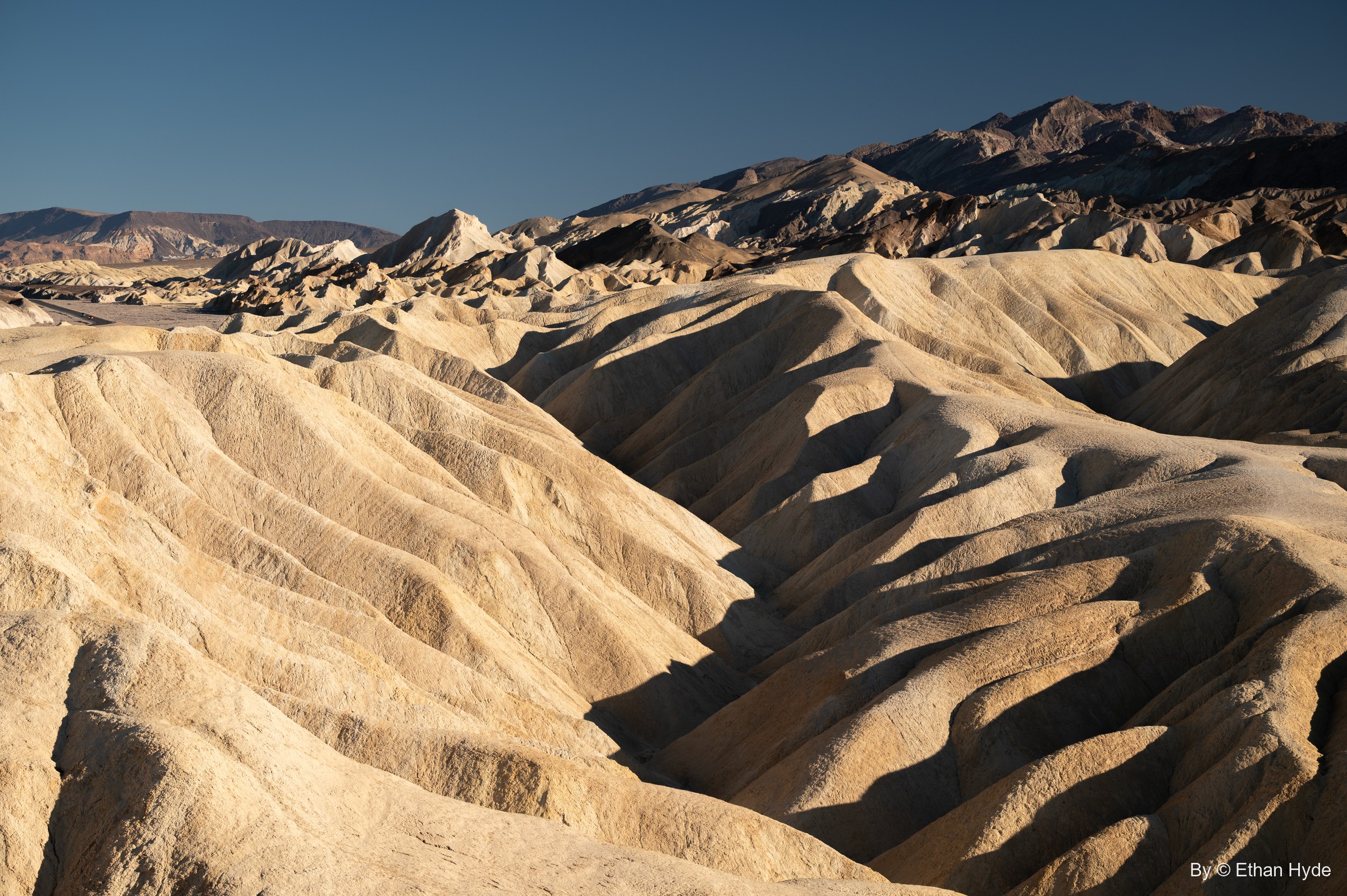 Deep gullies cut through golden badland ridges at Zabriskie Point, with jagged peaks on the skyline.