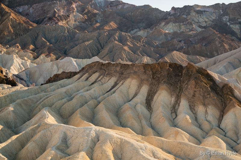 A ridge capped with dark rock streaks down over cream-colored badlands at Zabriskie Point.