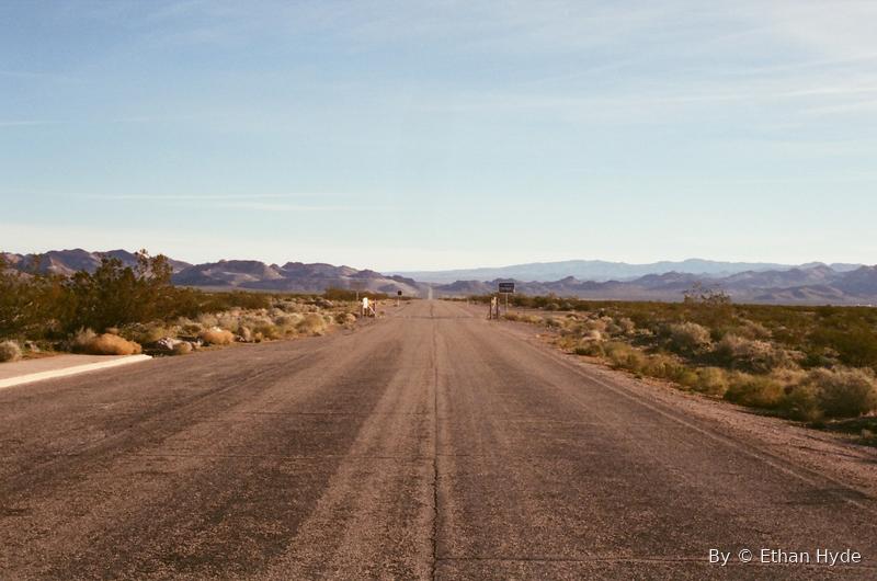 A dirt road running straight through open desert toward distant mountains.