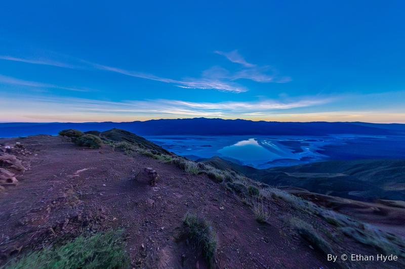 A wide desert valley seen from a ridge at dusk, mountains fading into blue.
