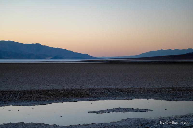 A shallow pool on the Badwater salt flat holds the pink and blue dusk sky beneath distant mountains.
