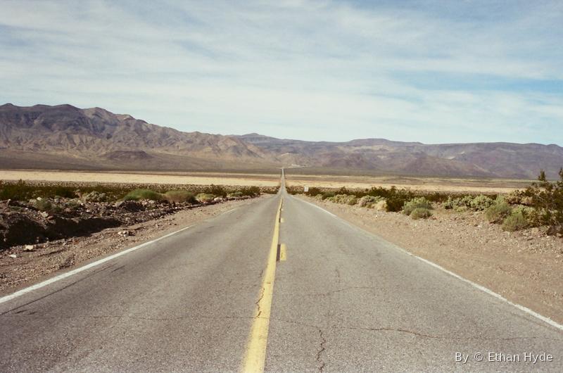 A desert highway with a yellow centerline running straight to distant mountains.
