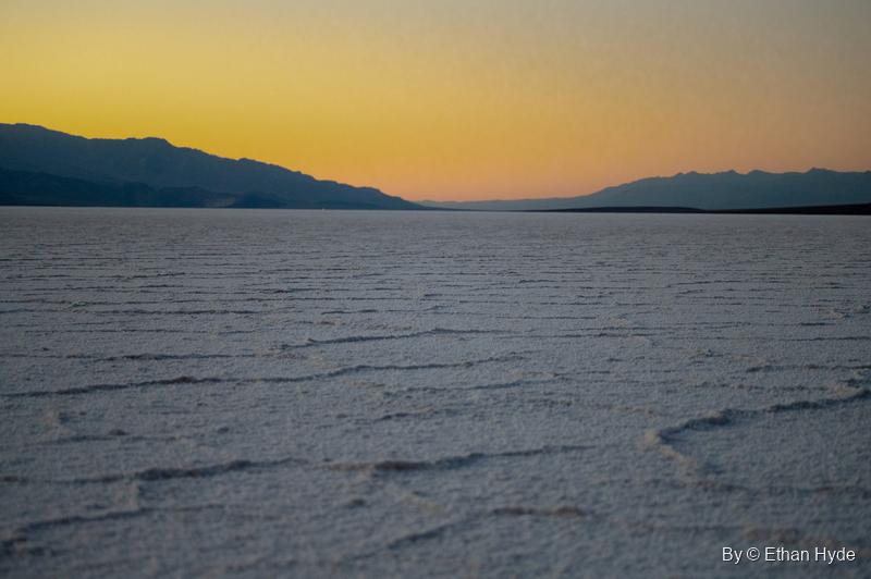 Ridged salt polygons stretch across Badwater Basin under an orange afterglow and a dark mountain silhouette.