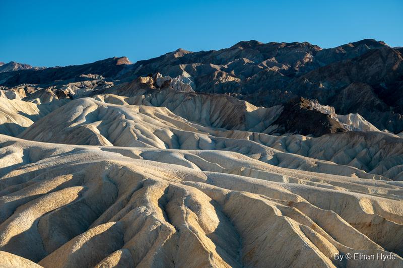 Rows of rounded yellow badland ridges at Zabriskie Point under the dark Black Mountains and a blue sky.