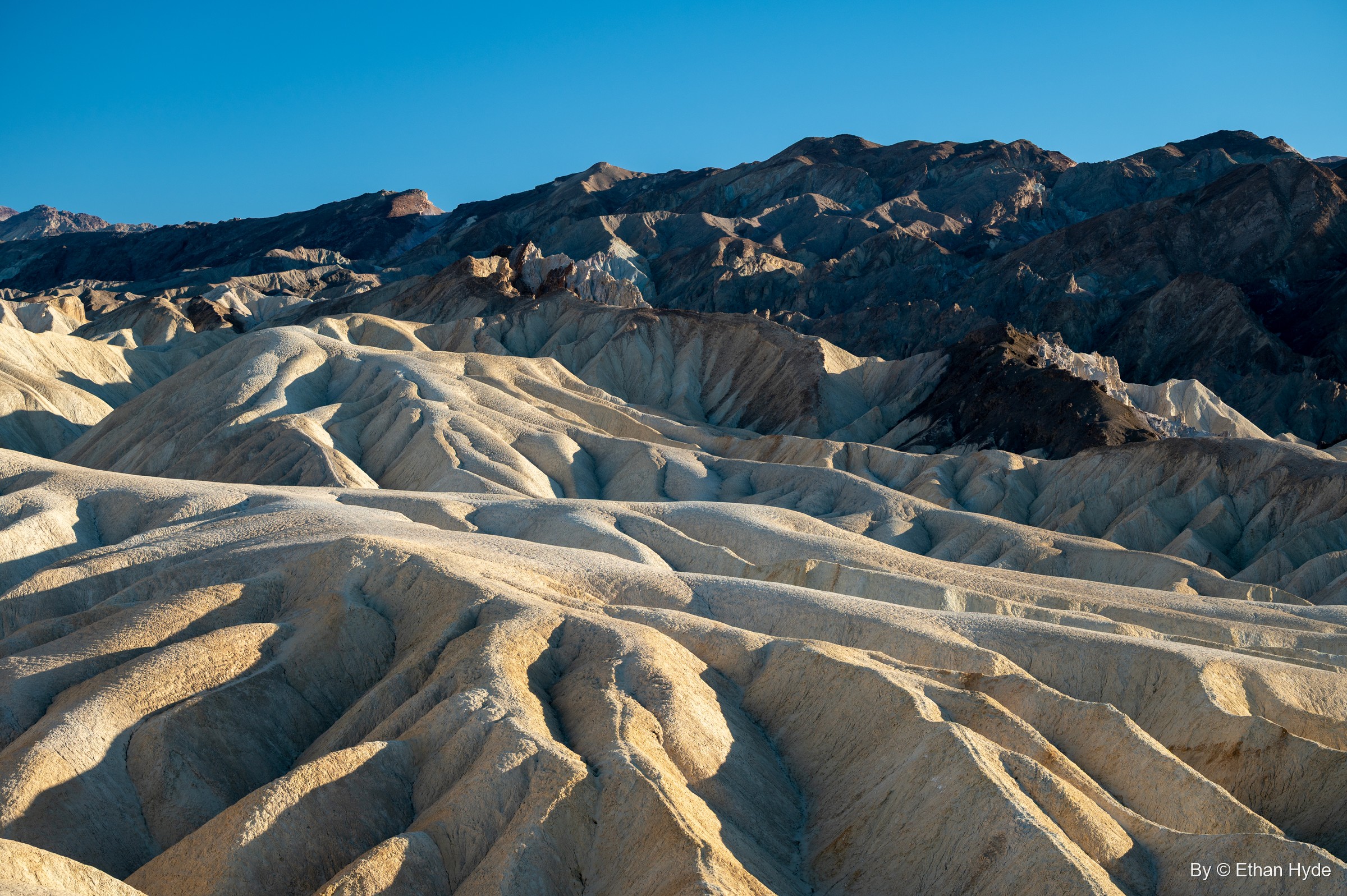 Rows of rounded yellow badland ridges at Zabriskie Point under the dark Black Mountains and a blue sky.