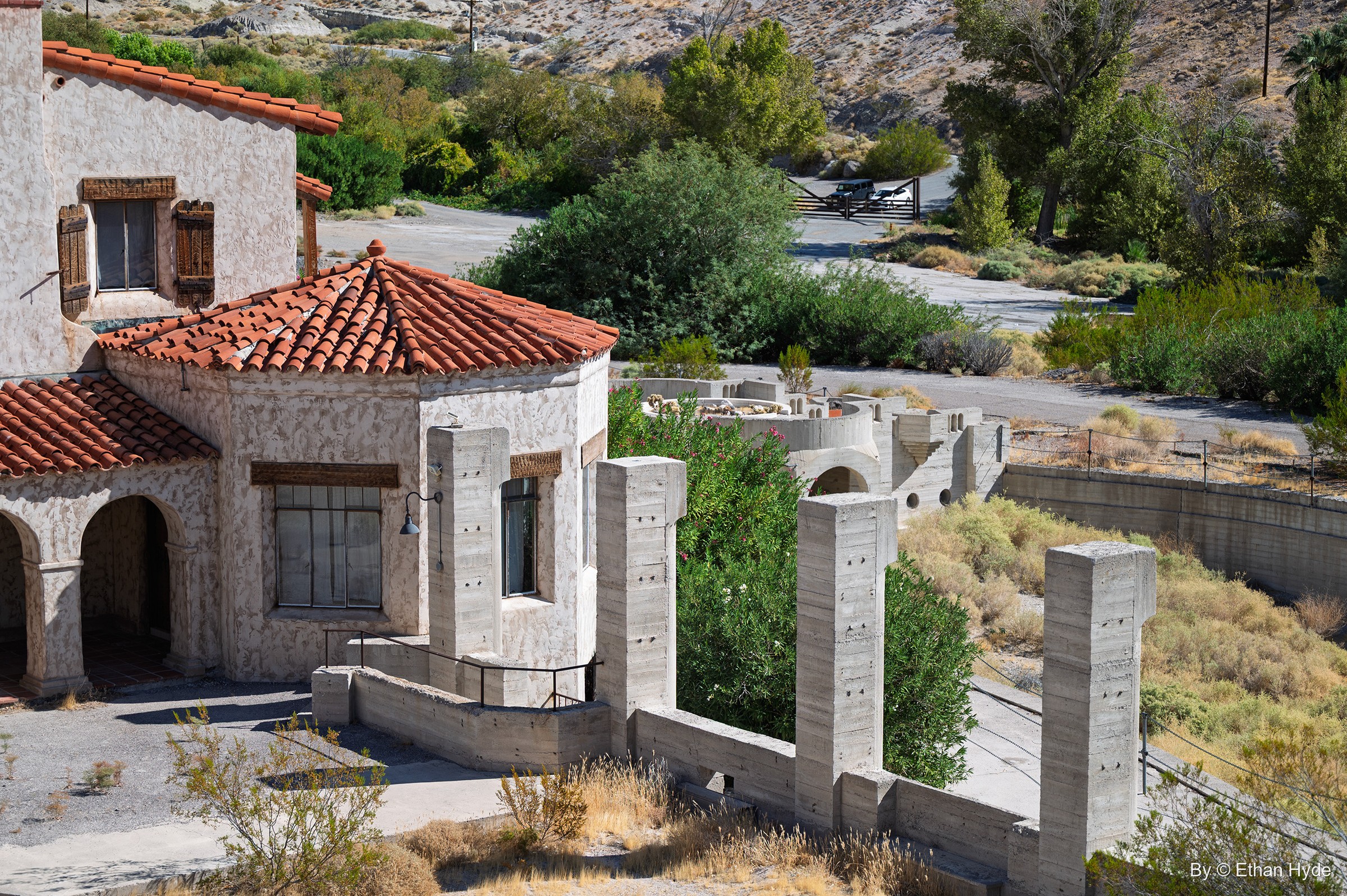 An elevated view over a round tile-roofed building and stucco walls at Scotty's Castle toward the green oasis of Grapevine Canyon.