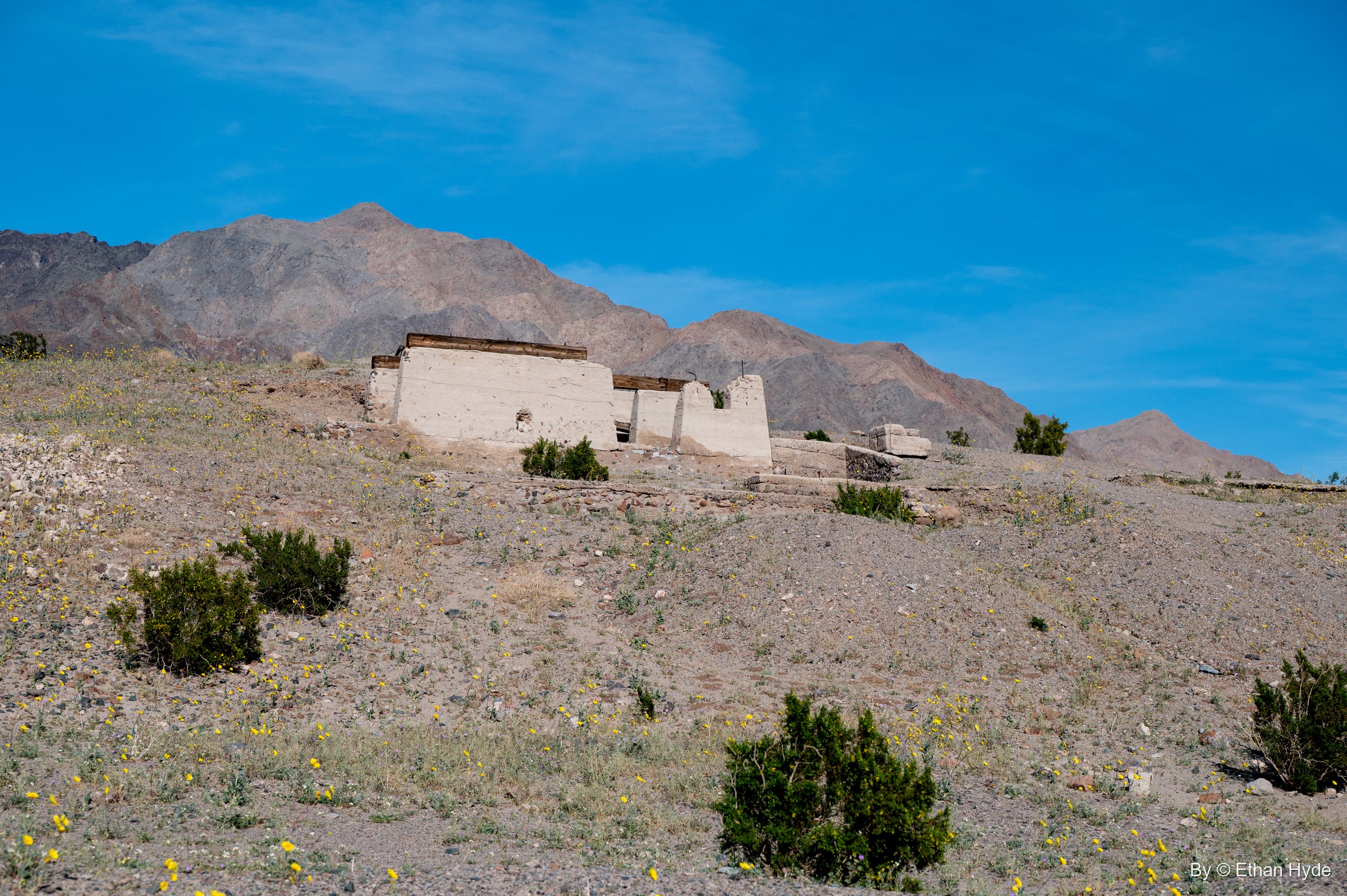 Crumbling concrete walls of the Ashford Mill office on a scrubby hillside below rugged mountains.