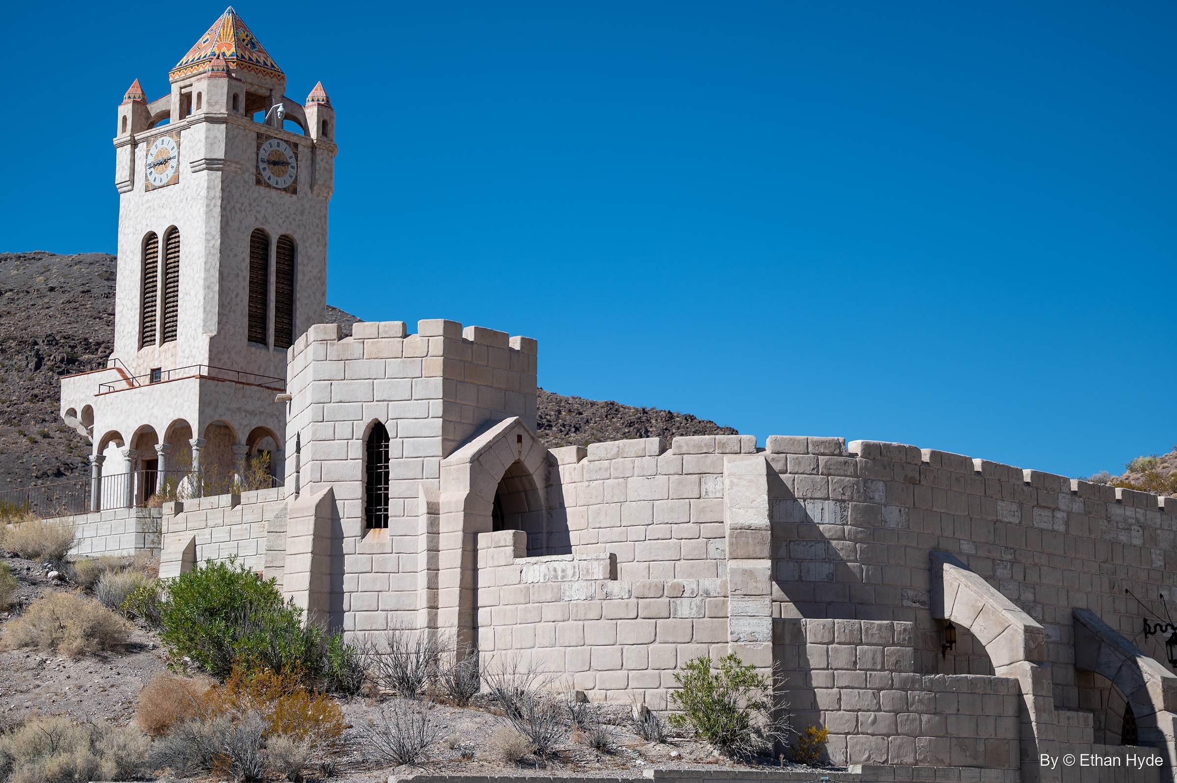 The Chimes Tower at Scotty's Castle above crenellated stone-block walls on a dry desert slope.