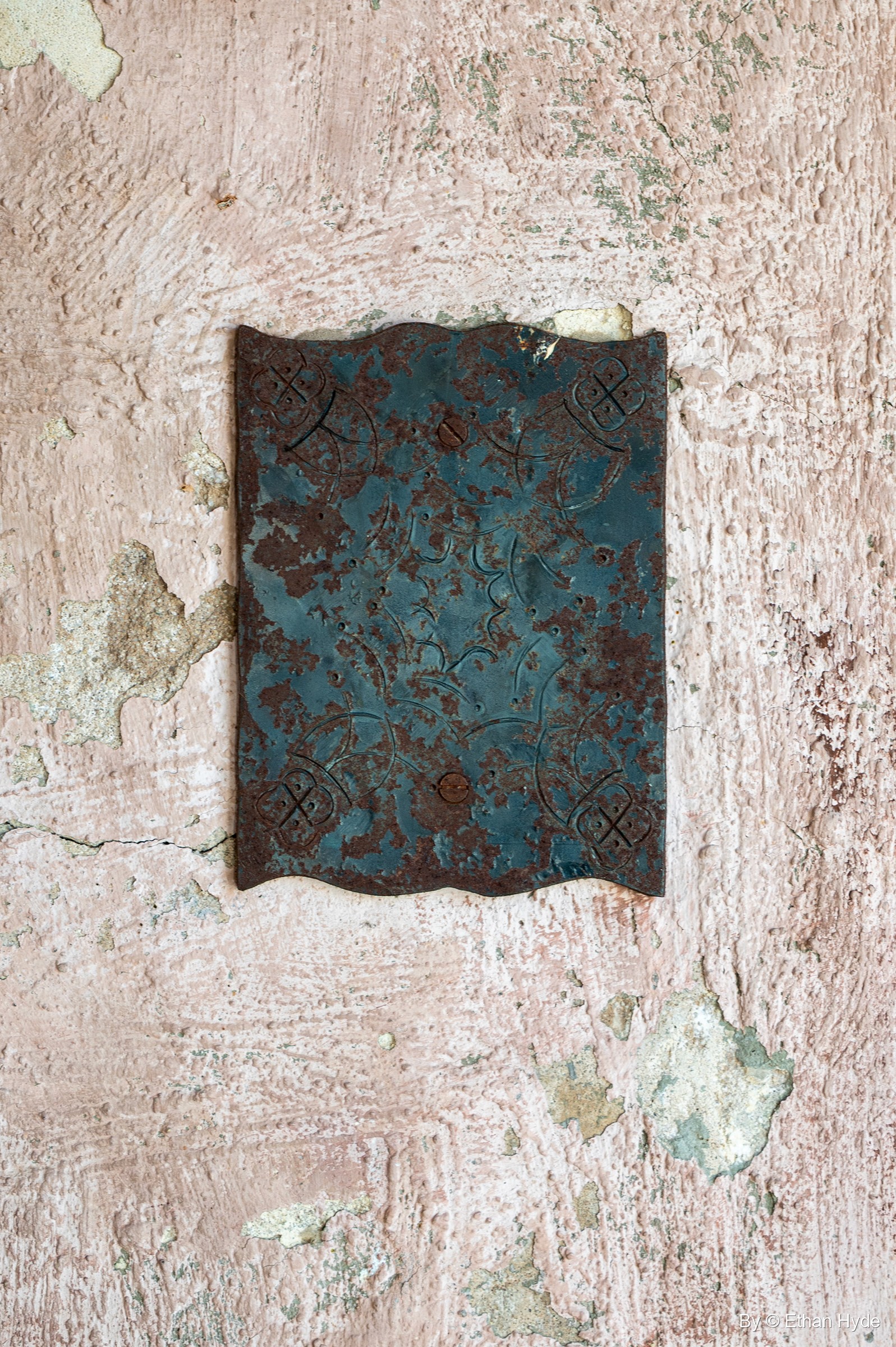 A weathered blue-green plate with a faint pattern on a peeling stucco wall at Scotty's Castle.