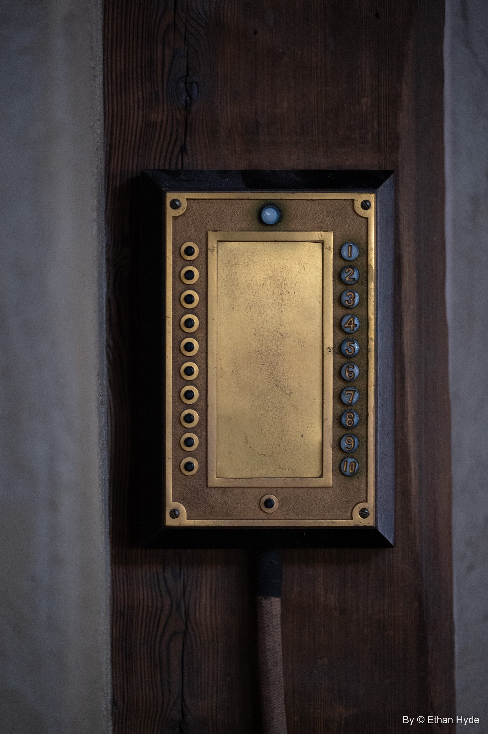 A brass servant call-button (annunciator) panel on a dark wooden post, Scotty's Castle.