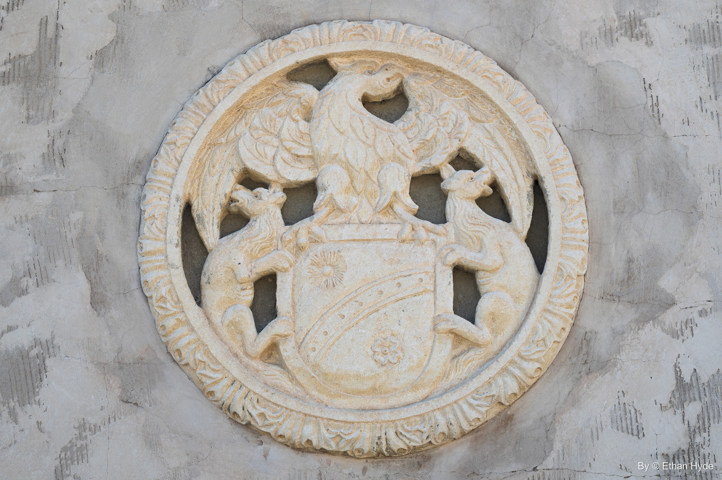 A carved circular medallion of a coat of arms with an eagle crest and two heraldic animals, set into a stucco wall at Scotty's Castle.